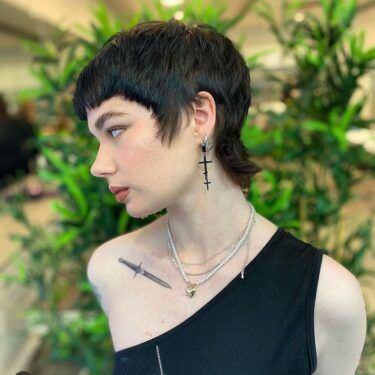 A side profile of a woman with a short mullet hairstyle and long, dangling earrings