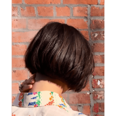 The back view of a woman with a blunt cut short bob hairstyle as she touches her neck