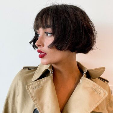 A side profile of a woman wearing a trench coat and red lipstick with a micro bob with bangs