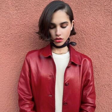 a close up of a woman with a leather jacket, a neck tie, red lip stick and a short, sleek bob