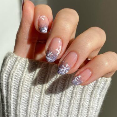 A manicure with silver glitter polish and snowflakes on the tips.