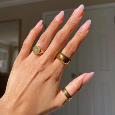 A manicured hand with baby pink polish and gold rings