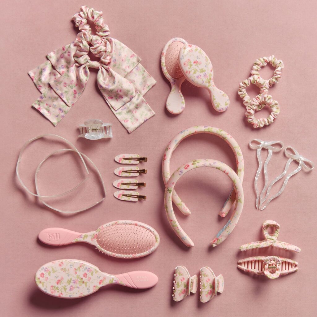 Hill House Home x Wet Brush collaboration featuring pink floral-print hair accessories and brushes—including scrunchies, headbands, claw clips, snap clips and Wet Brush hairbrushes—arranged on a pink background.