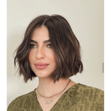 A woman wearing a short bob hairstyle with a middle part and a layered necklace