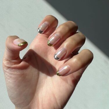 A close up of a woman's hands with bent fingers showcasing her manicured nails of mixed metal colors